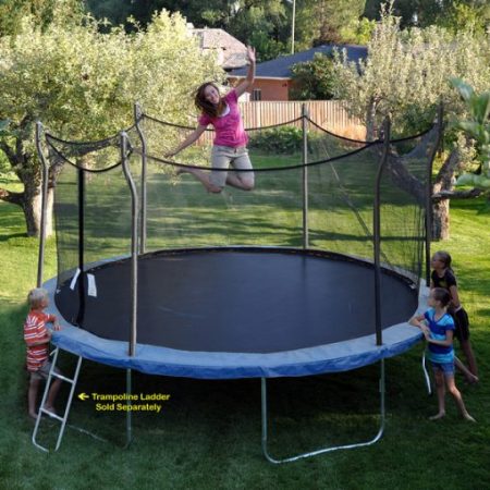 Brunette mom, with kids watching, jumps on a blue Propel Trampoline in backyard
